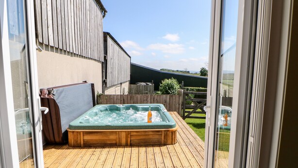 Eine Holzterrasse mit Whirlpool und einem Holzzaun im Hintergrund.