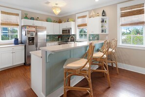 Una cocina con armarios blancos, una isla central, sillas de mimbre y vistas al exterior.