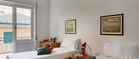 A room with two beds, a wooden nightstand, a sewing machine, and framed pictures on the wall.