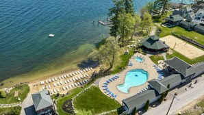 Vue aérienne d’un complexe hôtelier au bord d’un lac, avec une piscine, une plage et de nombreuses chambres.