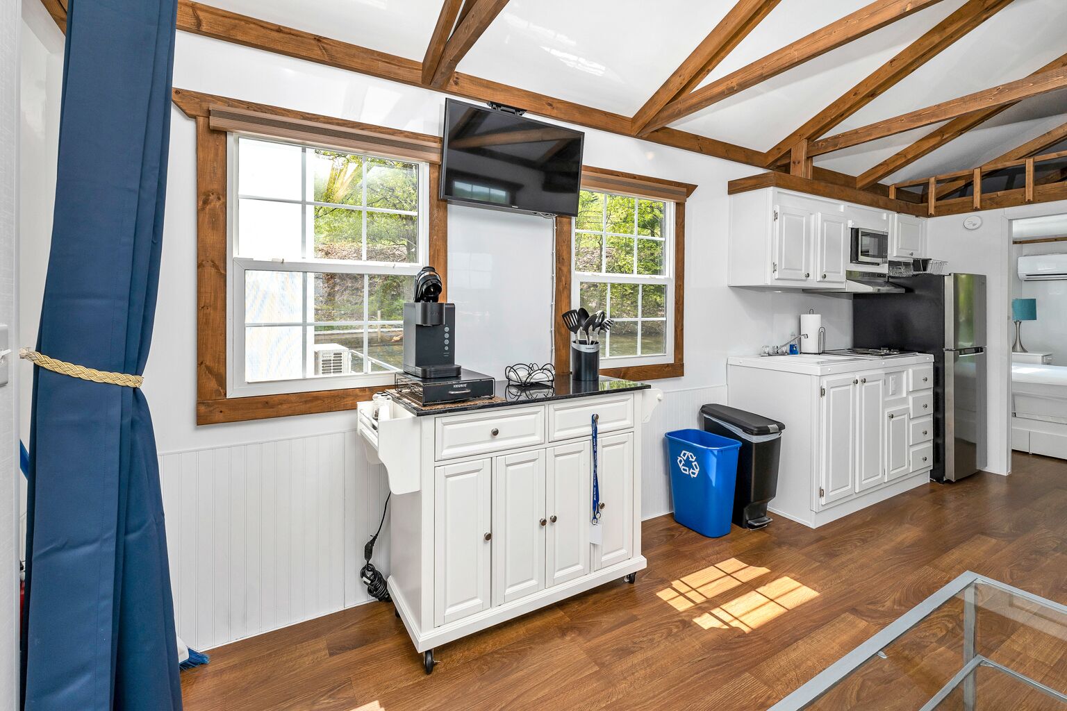 A kitchen with white cabinets, wooden beams, a coffee machine, and a trash bin.