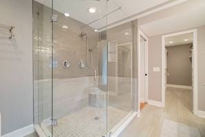 A modern bathroom with a glass-enclosed shower, tiled walls, and a wooden floor.
