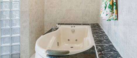 Un baño con una bañera independiente, paredes de azulejos y una zona de ducha decorativa.