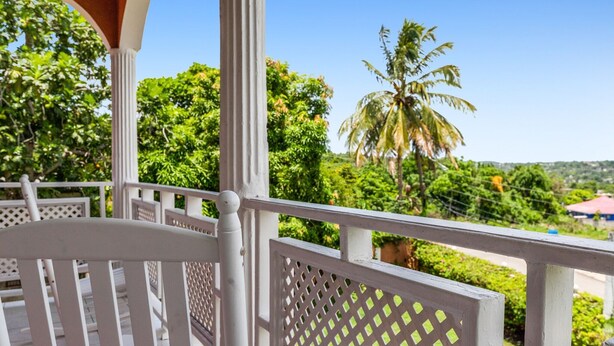 A balcony with white railings and a view of lush greenery and a palm tree. - YanceyLargo- 4BR Villa Jacuzzi & Mountain Views by RedAwning (Montego Bay)