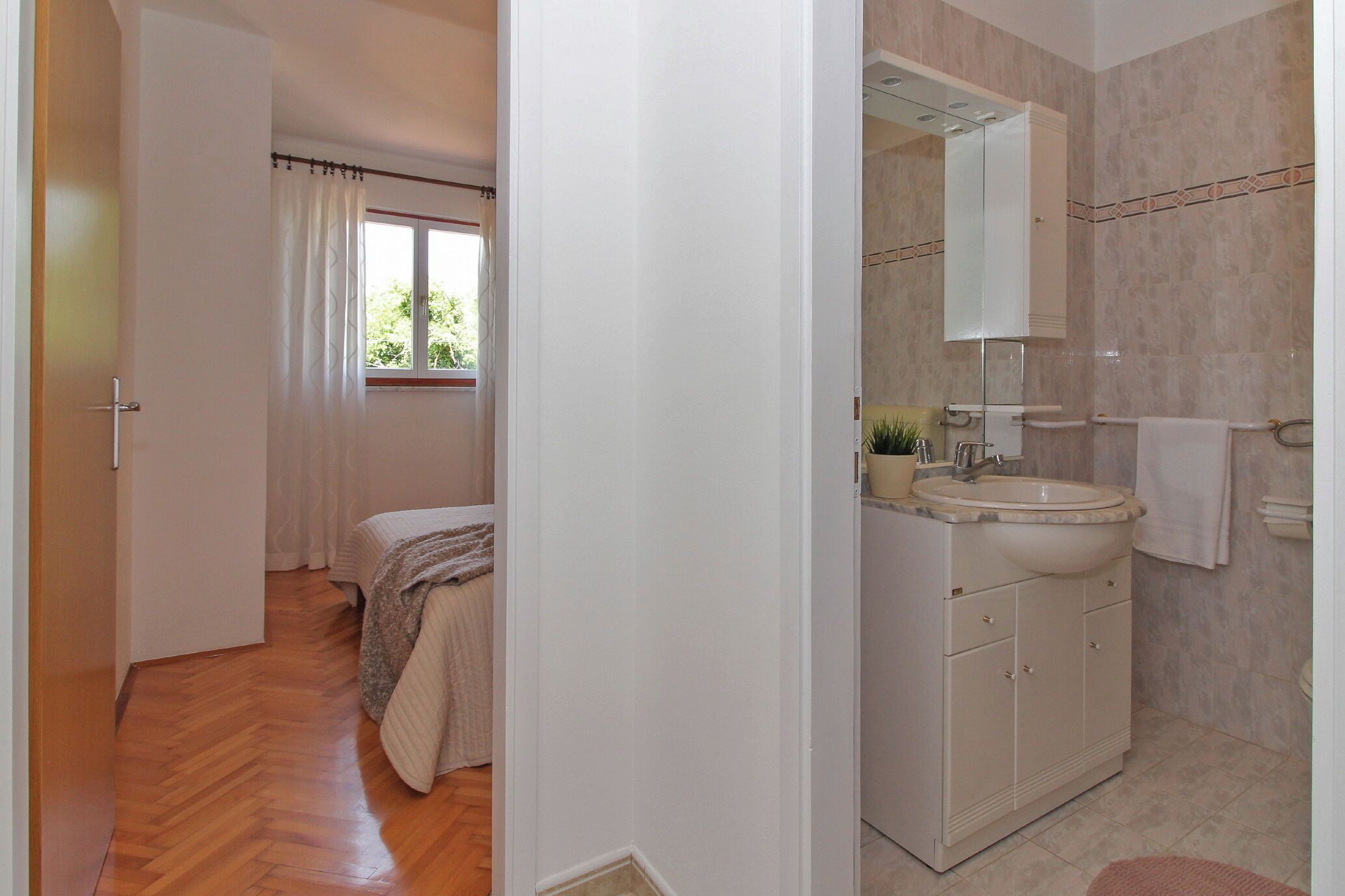 A bedroom with a bed, a bathroom with a sink and mirror, and a hallway with a door.