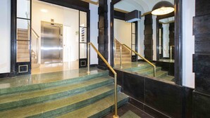 Uma escadaria imponente com corrimão, que leva a um elevador e a uma porta com o sinal 'P', indicando estacionamento.