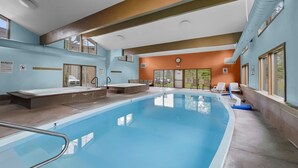 Une piscine intérieure offrant une vue dégagée sur l’ensemble de l’espace piscine, une horloge au mur et un panneau d’avertissement également fixé au mur.