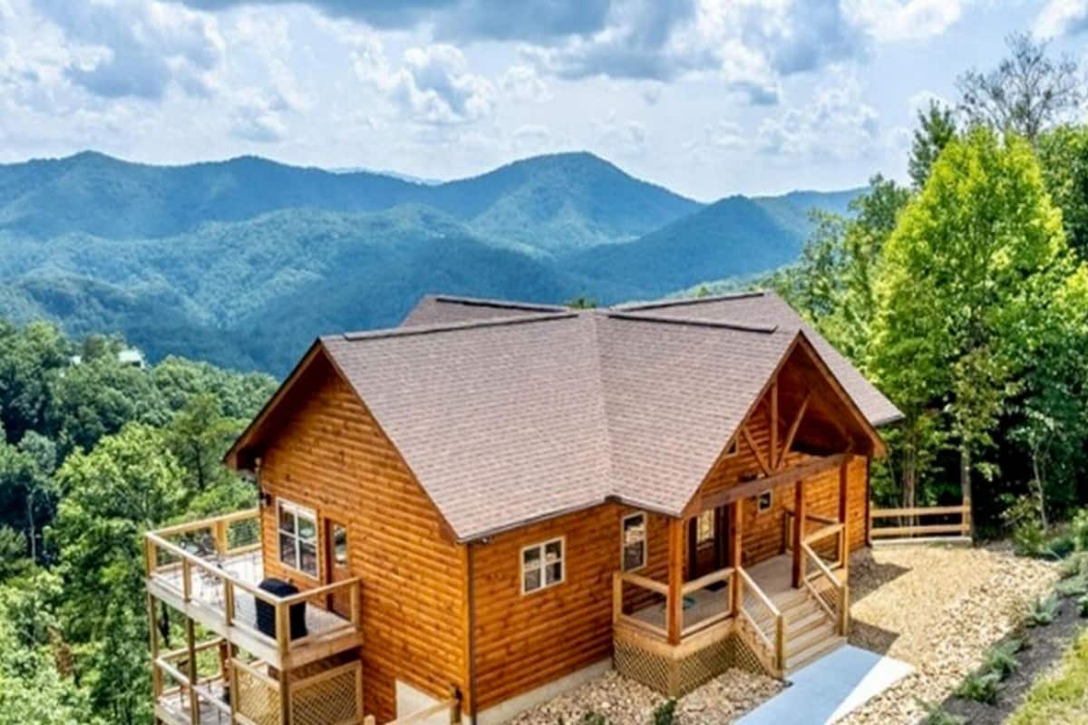 A wooden cabin with a balcony, surrounded by mountains and trees.