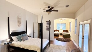 A spacious bedroom with a four-poster bed, a ceiling fan, and a large window with blinds.