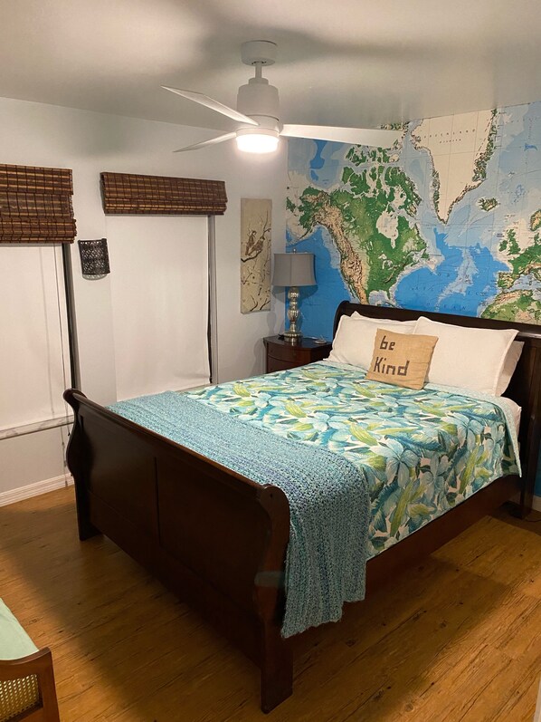 A bedroom with a bed, a map on the wall, a ceiling fan, and a nightstand with a lamp. - Spectacular Sunsets with Waterfront Views (Cape Coral)