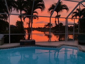 A swimming pool with a view of palm trees and a sunset over a body of water. - Spectacular Sunsets with Waterfront Views (Cape Coral)