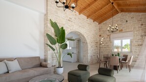 A spacious living area with a stone wall, a wooden ceiling, a sofa, a coffee table, and a dining area with chairs and a table.