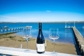 Una botella de vino y dos copas sobre una barandilla, con vista a una playa y el mar.