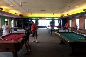 Une salle de billard avec plusieurs tables de billard, un mur vert et un drapeau américain.