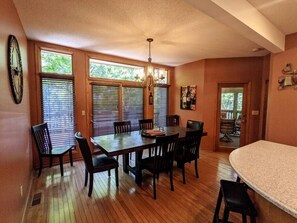 A dining area with a wooden table and chairs, a chandelier, and large windows with blinds. - Wonderful Home Away From Home, Wonderful Home Away From Home - with Hot Tub (Galena)