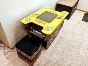 A small, yellow arcade machine with a control panel and a screen, placed on a carpeted floor next to a wicker basket. - Wonderful Home Away From Home, Wonderful Home Away From Home - with Hot Tub (Galena)