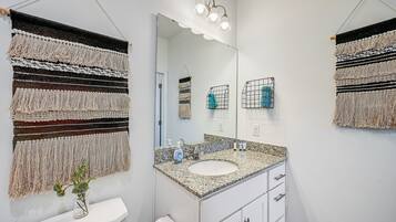 Un baño con un espejo grande, un lavabo con encimera de granito y un dispensador de papel higiénico.