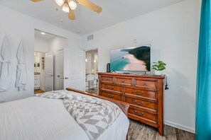 Un dormitorio con una cama, un aparador de madera, un televisor en la pared y un baño visible a través de una puerta abierta.
