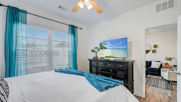 Un dormitorio con una cama, un ventilador de techo, un aparador y un cuadro de una playa.