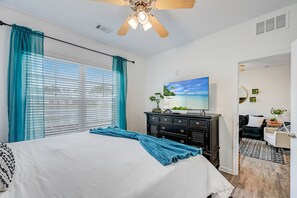 Un dormitorio con una cama, un ventilador de techo, un aparador y un cuadro de una playa.