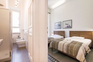 A hotel room with a shower, toilet, two beds, and two framed pictures on the wall.