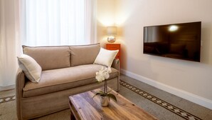 Un salon avec un canapé, une table basse ornée d’une plante, un téléviseur fixé au mur et une lampe.