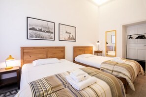 A hotel room with two beds, a wooden headboard, a nightstand with a lamp, a mirror, and two framed pictures on the wall.