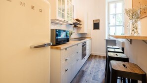 Une cuisine compacte avec un réfrigérateur blanc, un four à micro-ondes et un évier. On y trouve des tabourets en bois et une fenêtre avec vue.
