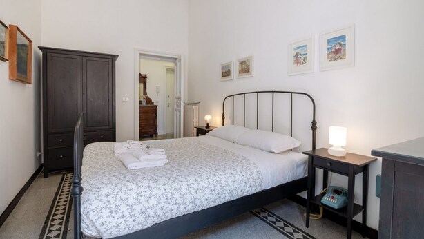 Une chambre à coucher avec un lit, une table de chevet avec une lampe, une commode et des tableaux encadrés au mur.