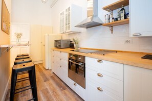 Una cocina moderna con armarios blancos, encimera de madera, campana de acero inoxidable y horno empotrado.