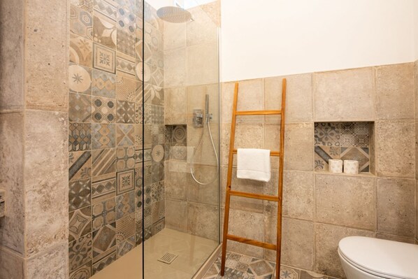A bathroom with patterned tiles, a glass shower enclosure, a wooden ladder, and a toilet.