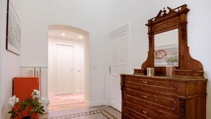 Un couloir avec une commode en bois, un vase rempli de fleurs et une porte donnant sur une autre pièce.