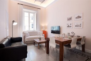 A modern living room with a sofa, a dining table with chairs, a TV, and framed pictures on the wall.