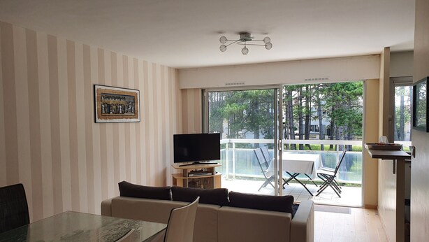 A living room with a glass table, a sofa, a TV, and a balcony with a table and chairs. - Le Touquet, Ap 67 m2, 2 Chambres, Secteur Quentovic, 5 min Plage et Centre (le Touquet Paris Plage)