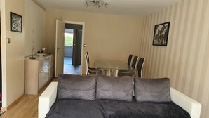 A living room with a white sofa, a dining table with chairs, and a kitchen area. - Le Touquet, Ap 67 m2, 2 Chambres, Secteur Quentovic, 5 min Plage et Centre (le Touquet Paris Plage)
