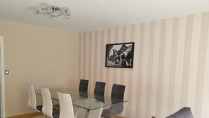A dining area with a glass table and chairs, a striped wall, and a framed picture. - Le Touquet, Ap 67 m2, 2 Chambres, Secteur Quentovic, 5 min Plage et Centre (le Touquet Paris Plage)