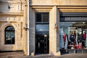 A building facade with a black door, a window with a tree reflection, and a storefront with mannequins and a Christmas tree display.
