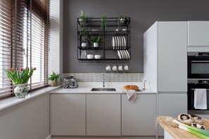 A modern kitchen with a built-in oven, a bread rack, and a window with blinds.