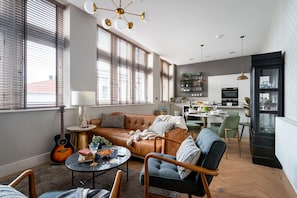 A modern living room with a leather sofa, a dining area, and a kitchen in the background.