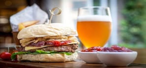 Un hamburger piqué d’un cure-dent, un verre de bière et deux petits bols de sauce sur une table en bois.