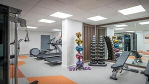Une salle de sport équipée de tapis de course, d’une zone d’entraînement avec des poids et d’un miroir qui reflète l’ensemble de la pièce.