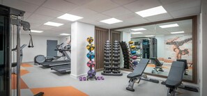 Une salle de sport équipée de tapis de course, de matériel de musculation et d’un miroir qui reflète l’espace.
