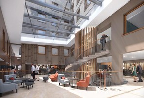 Eine geräumige Lobby mit einer zentralen Treppe, Sitzbereichen und einer hohen Decke mit Oberlichtern.