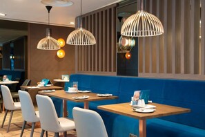 Ein Restaurant mit blauen Sitzelementen, weißen Stühlen und Pendelleuchten.