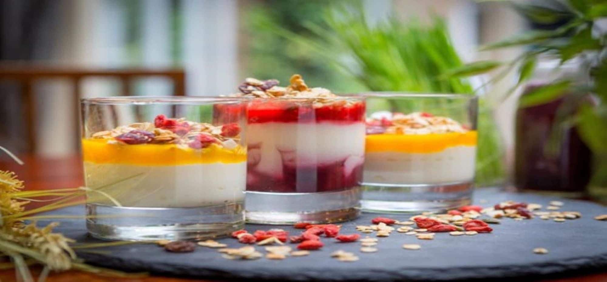 Three layered desserts in clear glasses with a dark surface underneath.