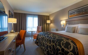 Une chambre d’hôtel avec un lit, un bureau, une chaise, une table et une fenêtre avec des rideaux.