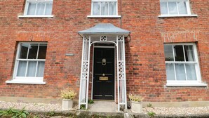 A red brick building with a black door, white windows, and a small porch with two potted plants.