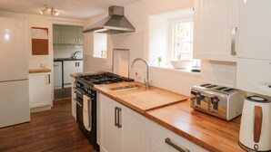 A modern kitchen with white cabinetry, a wooden countertop, a gas stove, a built-in oven, a sink, and a toaster.