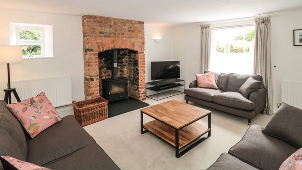 A living room with a brick fireplace, two sofas, a coffee table, a TV, and a window with curtains.
