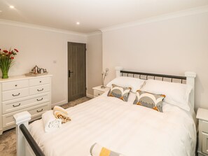 Quarto bem organizado com uma cama, mesas de cabeceira, cômoda e uma porta.